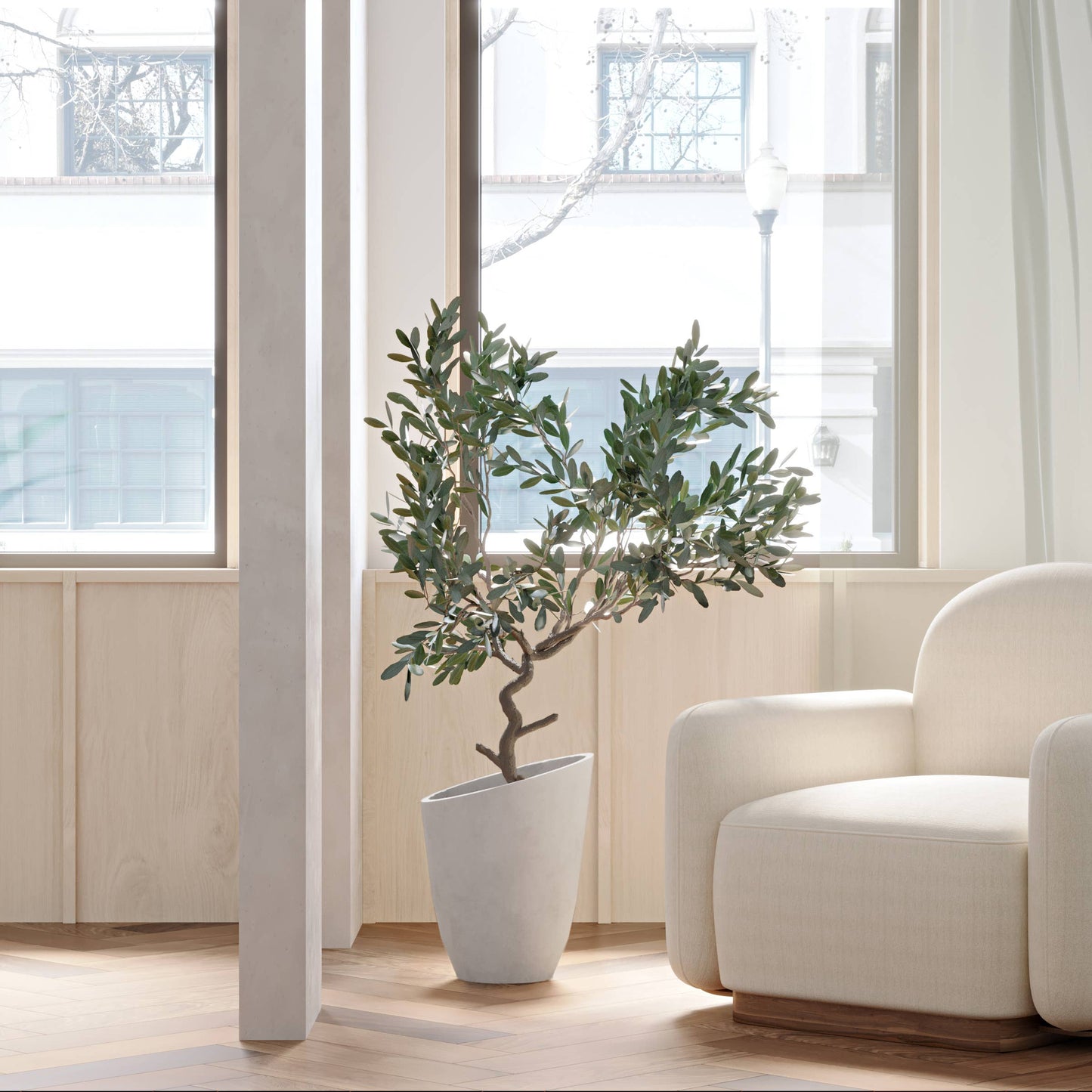 12-inch White Large Planter 'Chelsea' from Luxe Leaf Decor, featuring a large Olive tree, placed next to a white armchair in the corner of a bright, airy room.